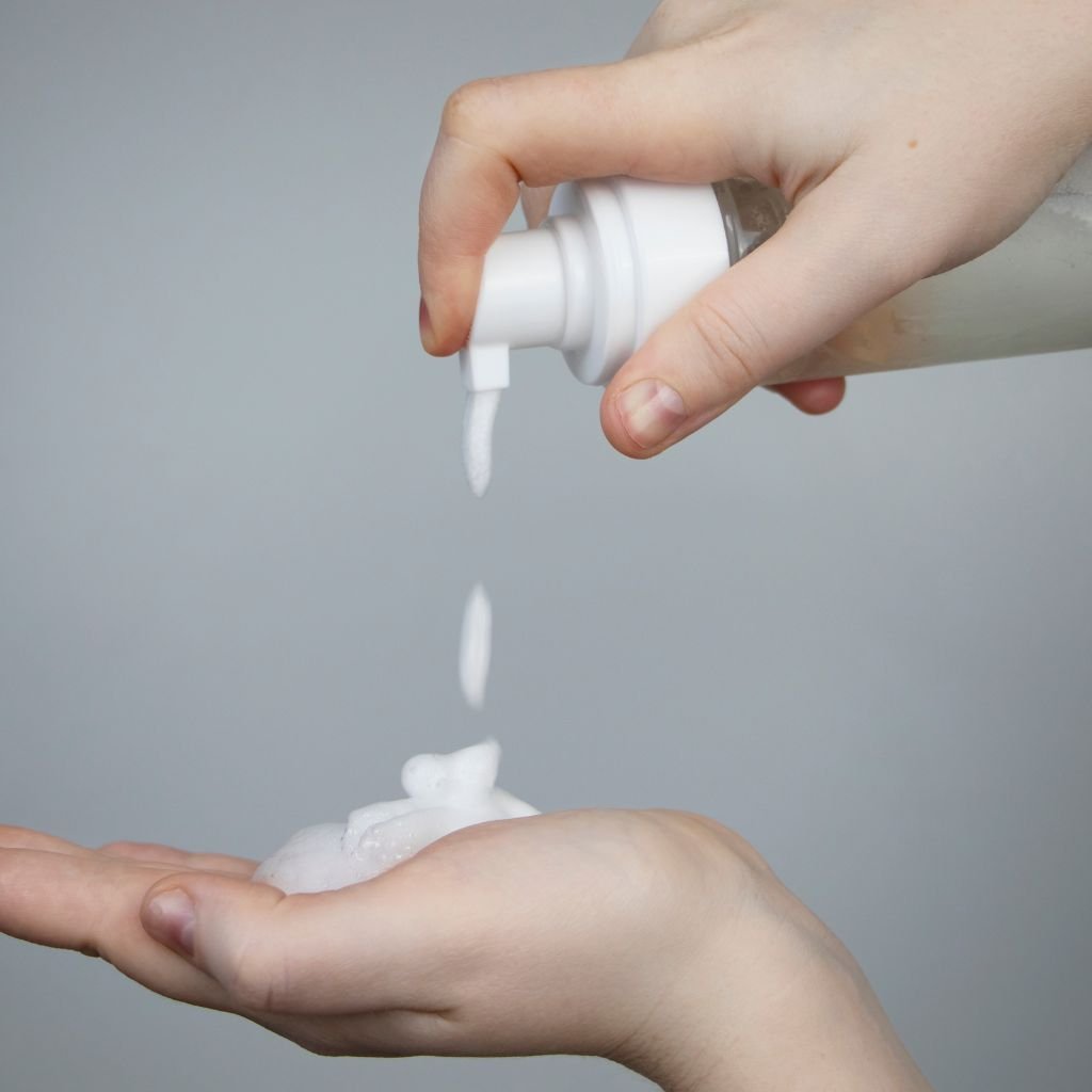 Close-up of hands dispensing foam from a pump bottle into the palm, representing the use of personal care or hygiene products, such as soap, lotion, or lubricant.