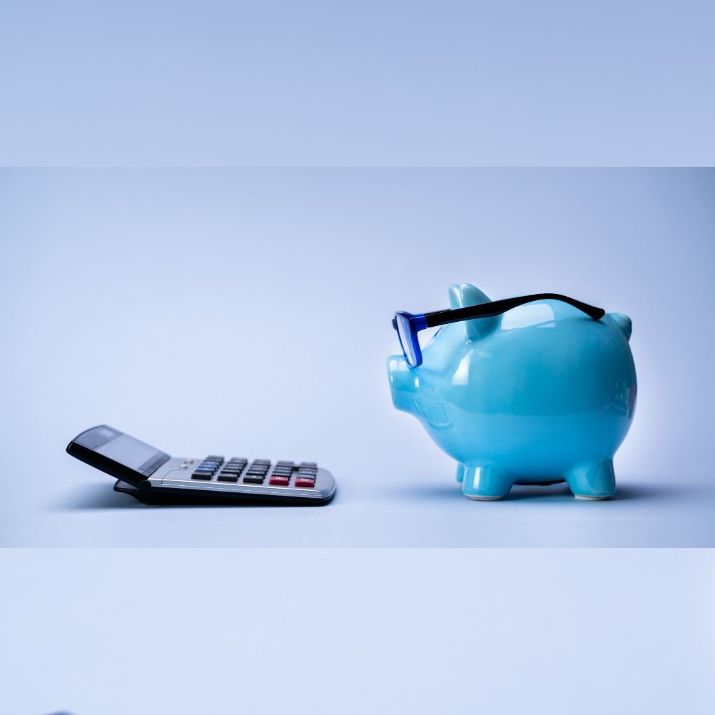 The image shows a playful representation of the concept of budgeting and quality. It features a blue piggy bank wearing glasses, symbolising financial prudence and smart decisions. The piggy bank is facing a calculator, reinforcing the theme of budget calculation or cost consideration. The minimalistic and light-coloured background adds a clean, focused vibe to the image, making it ideal for illustrating points about making cost-effective and informed choices while maintaining quality.