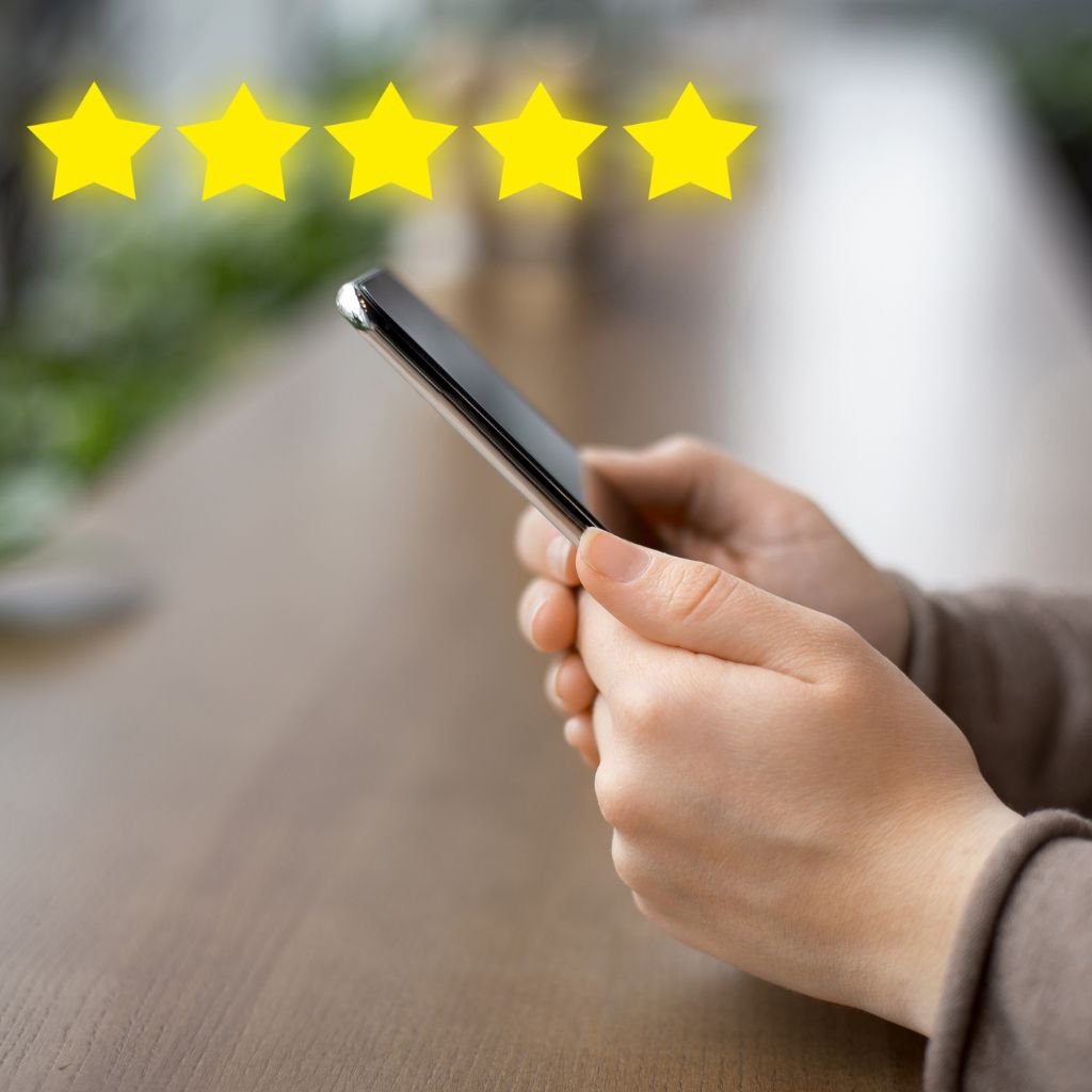 The image shows a person holding a smartphone with five bright yellow stars displayed above the phone. This symbolises a 5-star rating, commonly associated with high satisfaction or excellent reviews. The image visually conveys the concept of reading or giving reviews on a mobile device, suggesting the importance of customer feedback and ratings in decision-making. The background is slightly blurred, keeping the focus on the hands and phone while adding a modern, minimalist aesthetic.