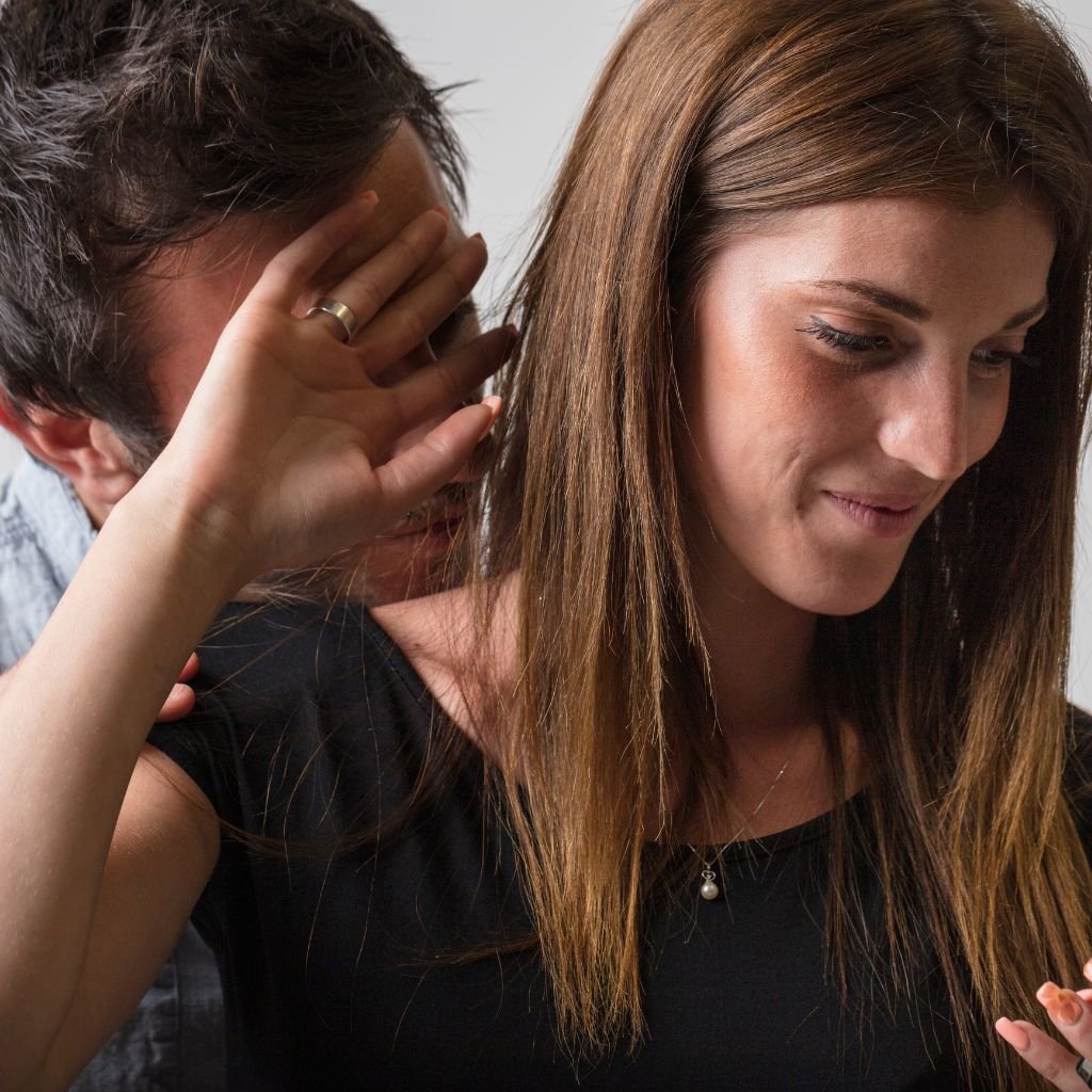 A close-up of a couple where the man leans in from behind, while the woman gently holds up her hand, creating space. She has a subtle smile, expressing the need to set a boundary while maintaining a warm atmosphere. The image illustrates the importance of respecting personal boundaries in a relationship.
